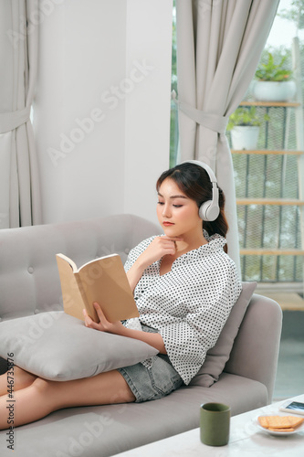 woman with headphones reading a book in the living room sitting on the couch