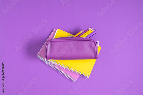 Purple pencil case with pencils and notebooks on purple background. Back to school. Flat lay, top view, copy space photo