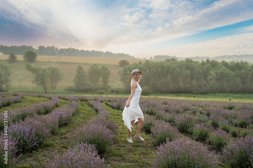 Beautiful young healthy woman with a white dress running joyfully through a lavender field, straw hat