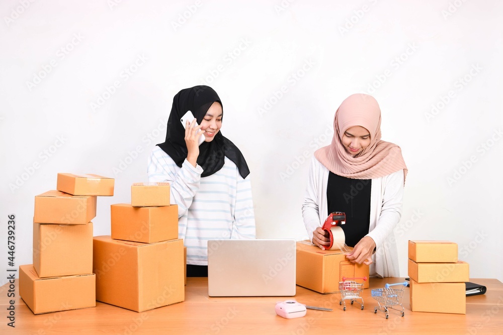 online business work Two beautiful colleagues work together. One girl is talking on the phone with a customer and the other is packing. in online selling with a smiling face. online business work Two beautiful colleagues work together. One girl is talking on the phone with a customer and the other is packing. in online selling with a smiling face.