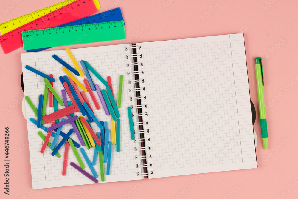 Open school squared notebook and colorful clips on the pink background. Blank white sheet of paper book on the table. Office supplies on the desktop. Back to school. Copy space for text. Top view Open school squared notebook and colorful clips on the pink background. Blank white sheet of paper book on the table. Office supplies on the desktop. Back to school. Copy space for text. Top view