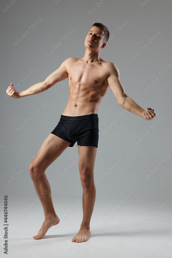 naked man in black panties on a gray background pumped up muscles of the torso barefoot 