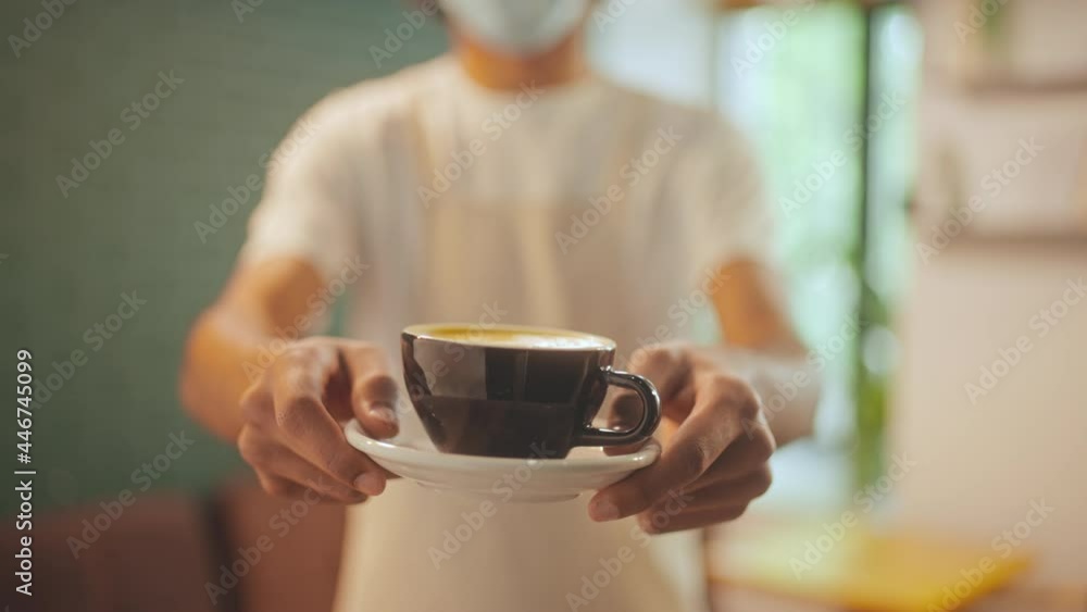 Waiter in protective mask offering cup of coffee to guest, restaurant service Waiter in protective mask offering cup of coffee to guest, restaurant service