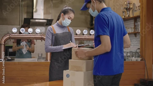 Asian delivery man wearing face mask for prevent coronavirus infection, deliver box of material to young woman restaurant owner or manager checking and receiving.