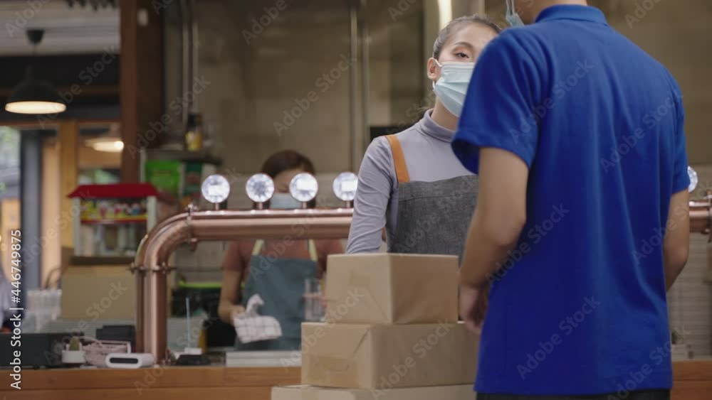 Asian delivery man wearing face mask for prevent coronavirus infection, deliver box of material to young woman restaurant owner or manager checking and sign for receive. Asian delivery man wearing face mask for prevent coronavirus infection, deliver box of material to young woman restaurant owner or manager checking and sign for receive.