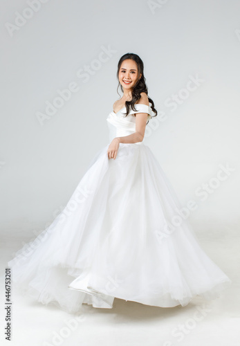 Full length of young attractive Asian woman  soon to be bride  wearing white wedding gown looking happy spinning. Concept for pre wedding photography