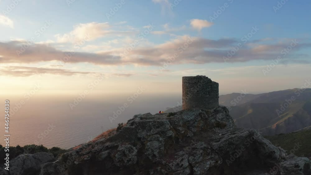 Beautiful panorama of aerial view of old and ancient building looking at the sea during sunset,green forest around.Two people on the top of mountain looking panorama,golden sea,clouds,mountain coast Beautiful panorama of aerial view of old and ancient building looking at the sea during sunset,green forest around.Two people on the top of mountain looking panorama,golden sea,clouds,mountain coast