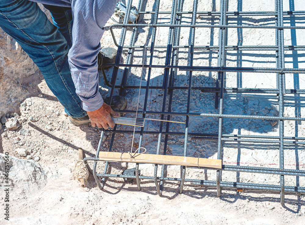 Construction worker checks the position of the reinforcing rods of a reinforced concrete foundation with a tape measure. Construction worker checks the position of the reinforcing rods of a reinforced concrete foundation with a tape measure.