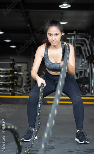 Powerful muscular woman exercising with battle ropes at the gym