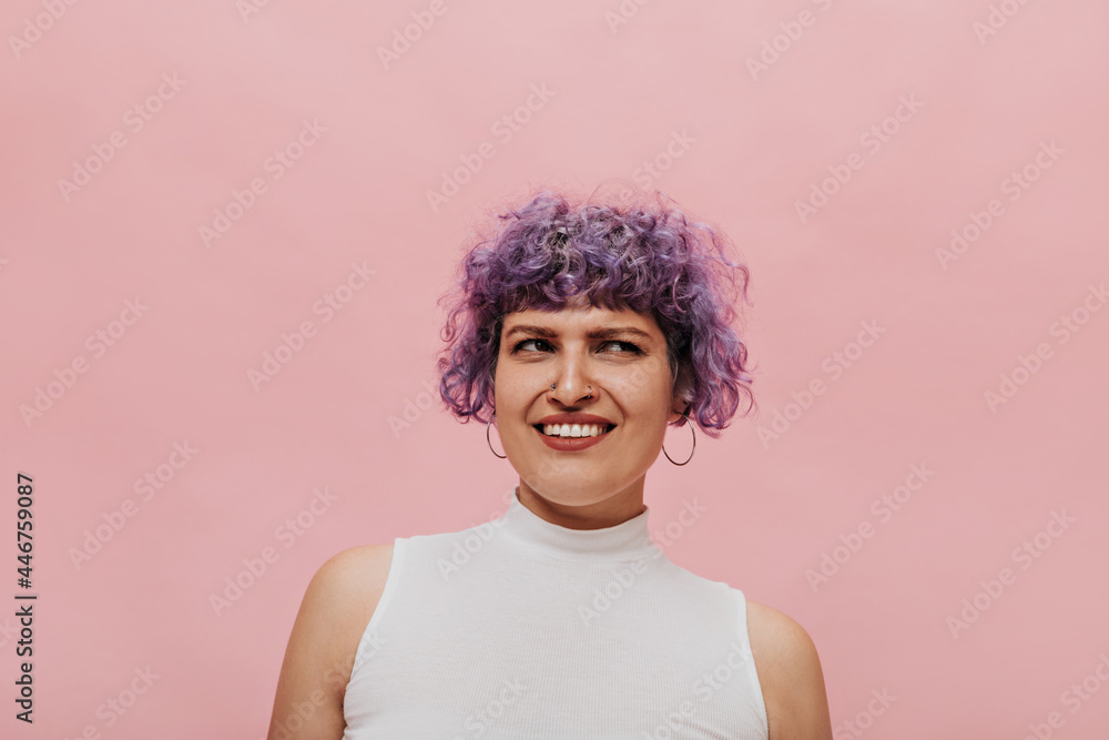 Photo of surprised adult girl with purple curly hair in white T-shirt. Beautiful woman in round earrings on pink background.. Photo of surprised adult girl with purple curly hair in white T-shirt. Beautiful woman in round earrings on pink background..