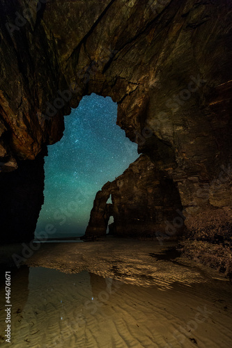imagen nocturna con un arco de piedra de la playa de las catedrales con las estrellas de fondo y el mar en los pies