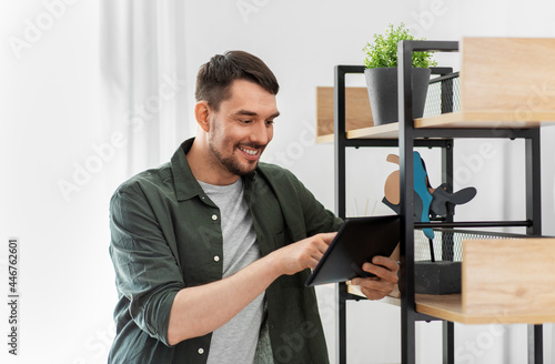home improvement and decoration and people concept - happy smiling man with tablet pc computer standing at shelf at home