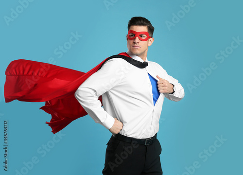 Businessman in superhero cape and mask taking shirt off on light blue background photo