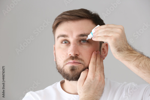 Young man using eye drops on light grey background