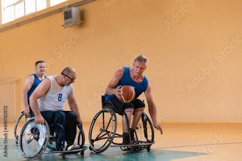Disabled War veterans mixed race opposing basketball teams in wheelchairs photographed in action while playing an important match in a modern hall.  © .shock