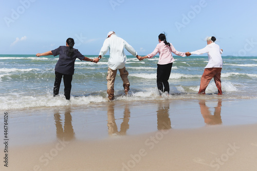 Group of four cheerful elderly old senior friends travel outdoor together, holding hands while standing on topical beach, have fun and enjoy spend time, resting and relaxing on holiday vacation. © Stella
