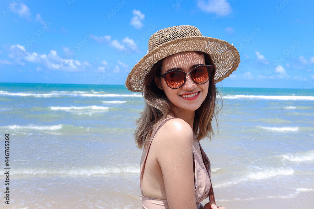 Portrait of beautiful Asian woman with big hat and sunglasses enjoy spending time on tropical sand beach blue sea, happy smiling female resting and relaxing on summer holiday vacation.