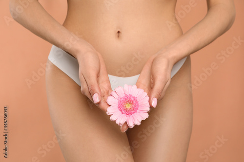 Woman in white panties with gerbera flower on peach background, closeup photo