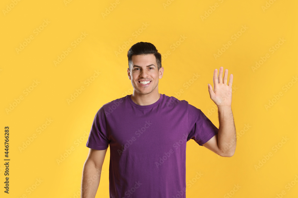 Cheerful man waving to say hello on yellow background Cheerful man waving to say hello on yellow background