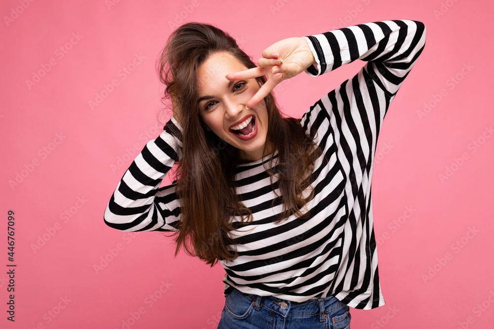 Fototapeta premium Photo of young european positive smiling winsome joyful happy beautiful brunette woman with sincere emotions wearing casual striped pullover isolated on pink background with copy space