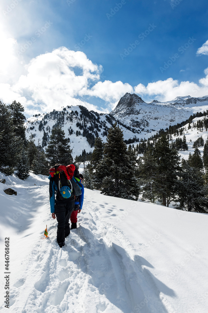 persona de ruta por la montaña con todo el paisaje nevado y el camino marcado por otras huellas, con montañas de fondo, el cielo azul y nubes 