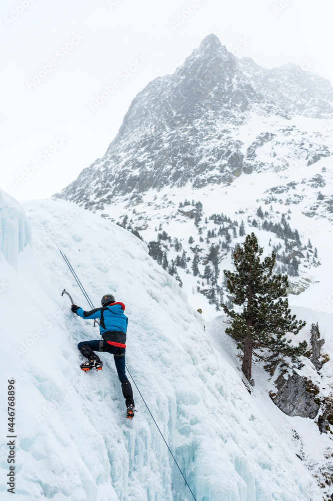 escalador en la cima de una cascada de hielo con la montaña al fondo