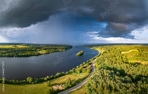  Impressive storm clouds over the river Daugava in warm sunny day. Aerial view over colorful crop fields and pine forest. 