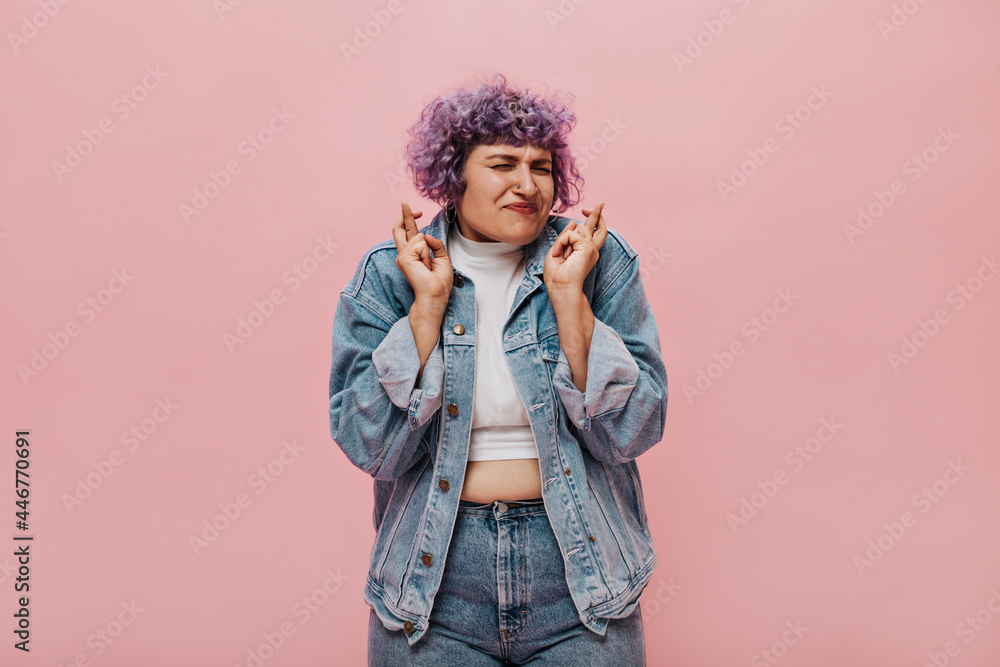 Fashionable lady in jeans outfit posing on pink isolated background. Wonderful girl with short lilac hair closed her eyes.. Fashionable lady in jeans outfit posing on pink isolated background. Wonderful girl with short lilac hair closed her eyes..