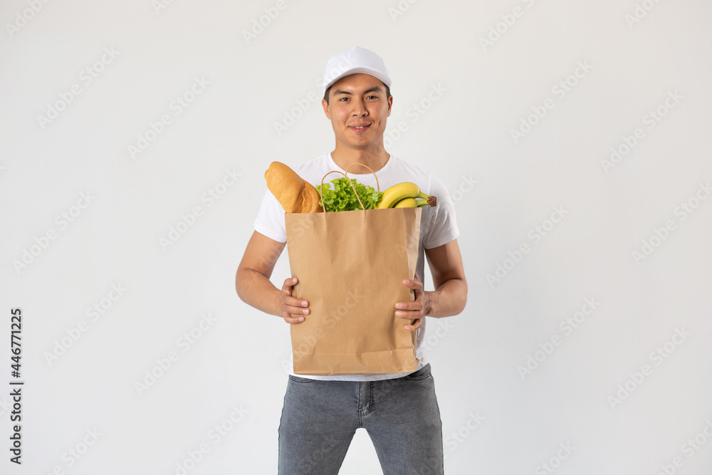 Asian delivery man in white cap holds craft bag with groceries on white background. Asian delivery man in white cap holds craft bag with groceries on white background.