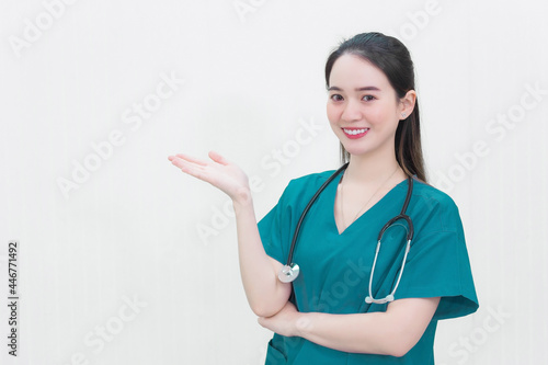 Beautiful young Asian woman doctor in a green uniform stands and smiles while pointing to the top on a white background.