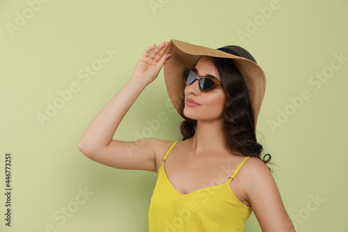 Beautiful young woman with straw hat and stylish sunglasses on light green background