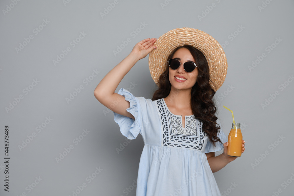 Beautiful young woman with straw hat and bottle of refreshing drink on light grey background. Space for text Beautiful young woman with straw hat and bottle of refreshing drink on light grey background. Space for text