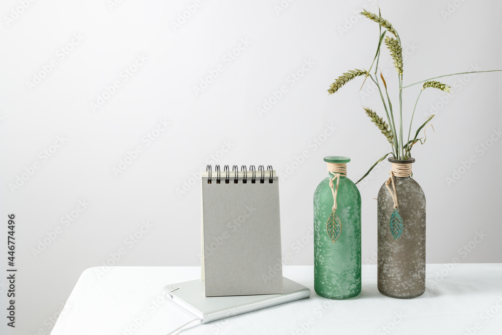 Calendar or reminder mockup with natural wheat spikelets in glass retro vase bottle on white table cloth against light wall. Home minimal vintage interior decoration Calendar or reminder mockup with natural wheat spikelets in glass retro vase bottle on white table cloth against light wall. Home minimal vintage interior decoration