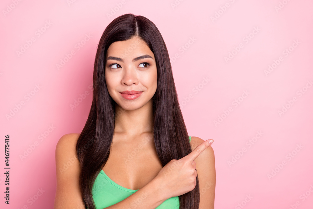 Photo of thoughtful pretty young lady wear green tank-top looking pointing finger empty space smiling isolated pink color background Photo of thoughtful pretty young lady wear green tank-top looking pointing finger empty space smiling isolated pink color background