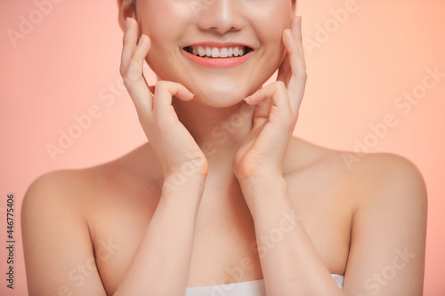 Cute young smiling woman touches her clean skin, on biege background