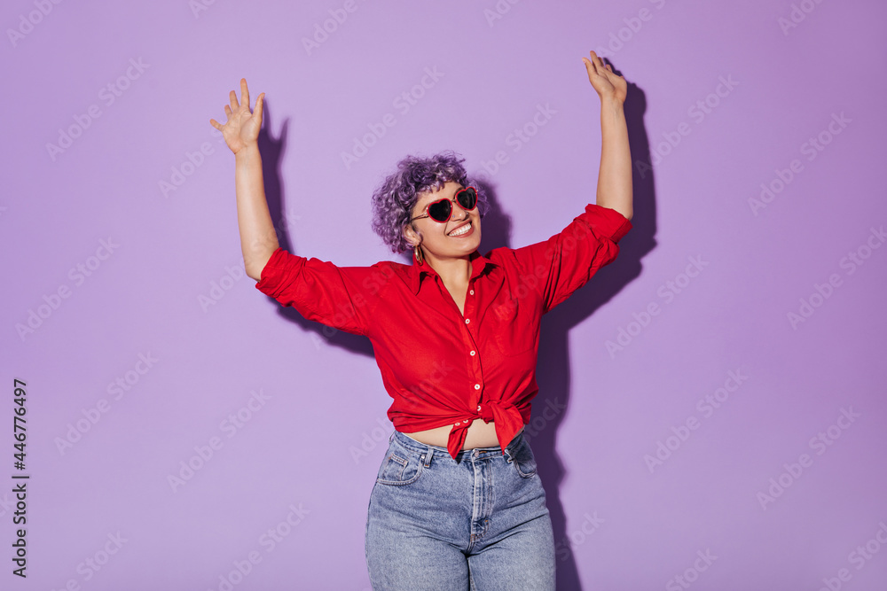 Charming adult girl with short hair and glasses in good mood in stylish clothes raises her hands and smiles on isolated background.. Charming adult girl with short hair and glasses in good mood in stylish clothes raises her hands and smiles on isolated background..
