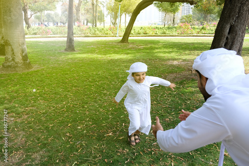 Arab young boy runs towards his Arabic father. Handsome cute Middle Eastern kid model plays with his parent wearing Kandora dish dash. Happy Emirati national family photo