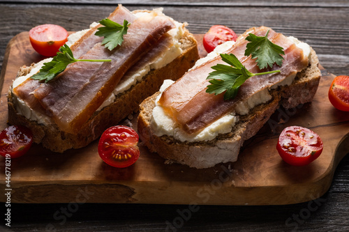 Sandwich with smoked fish, tomatoes, cream cheese on bread, on a dark wooden table.