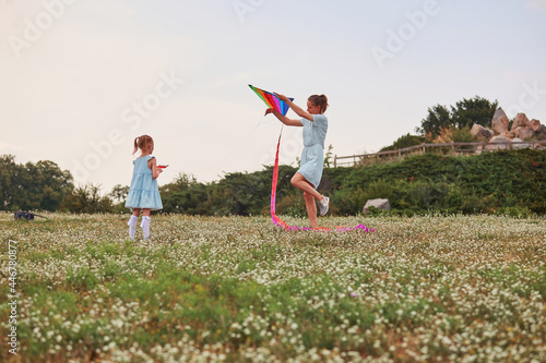 Fotografija Young mom with a little daughter play with flying a kite in a green park happy family having fun together