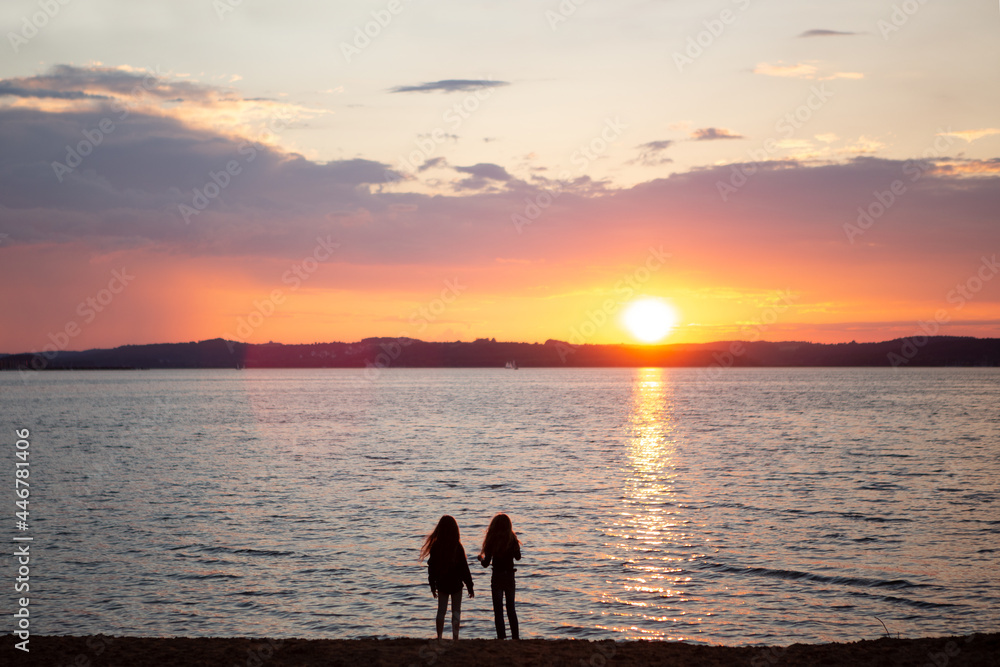 Two girls watching the sunset at lake