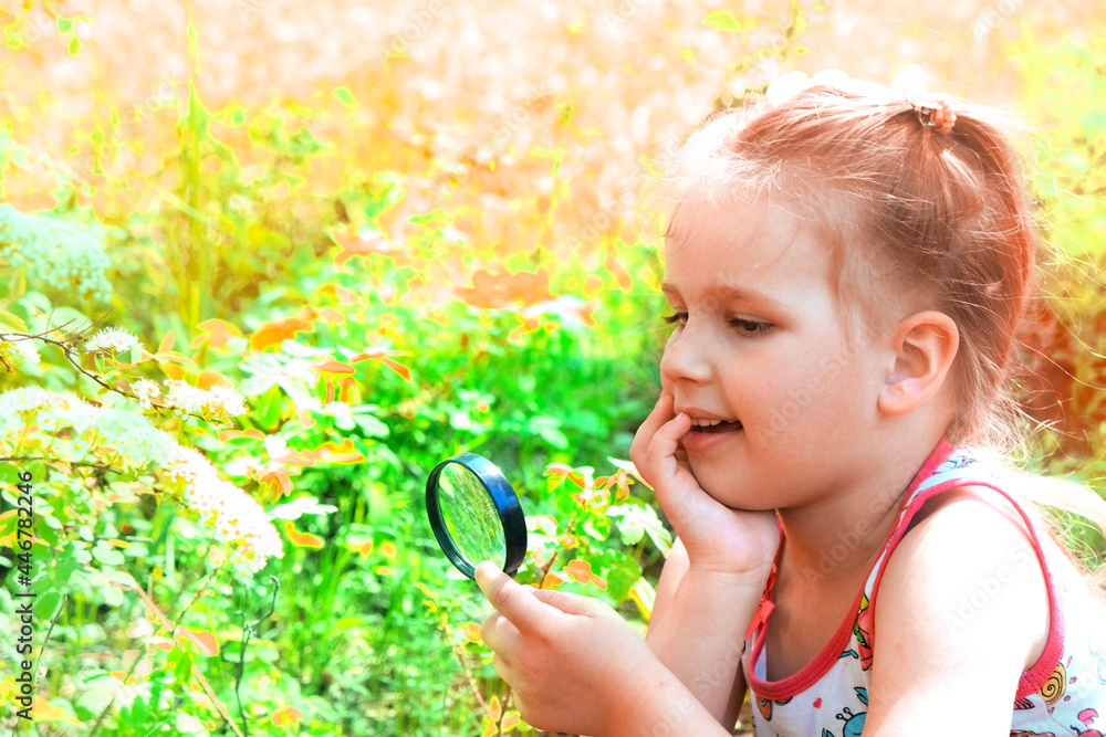 Little girl with a magnifying glass in her hand investigate details of nature . Summer time outdoor kids activity and learning concept.