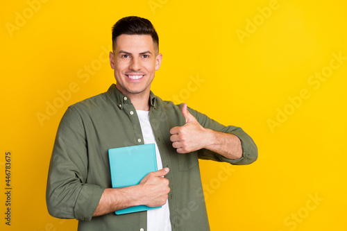 Photo portrait man smiling keeping book showing like thumb-up sign isolated vibrant yellow color background