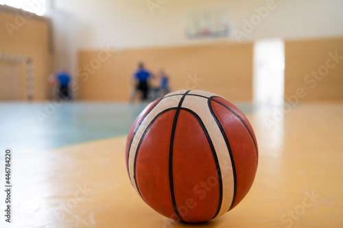 close up photo of a basketball on the court, in the background a sports team of people with disabilities preparing for a game