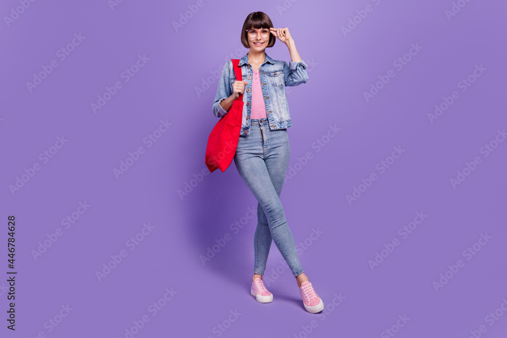 Full length photo of nice millennial brunette lady hold bag wear spectacles jeans shirt sneakers isolated on purple background Full length photo of nice millennial brunette lady hold bag wear spectacles jeans shirt sneakers isolated on purple background