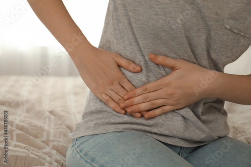 Woman suffering from appendicitis inflammation on bed at home, closeup