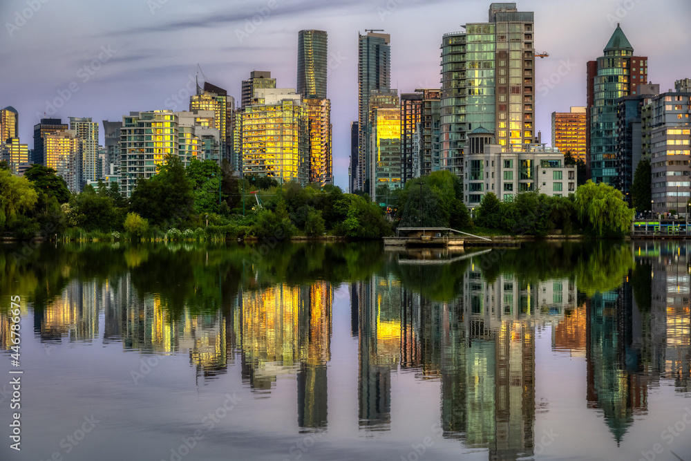 View of Lost Lagoon in famous Stanley Park in a modern city with buildings skyline in background. Colorful Sunset Sky. Downtown Vancouver, British Columbia, Canada.