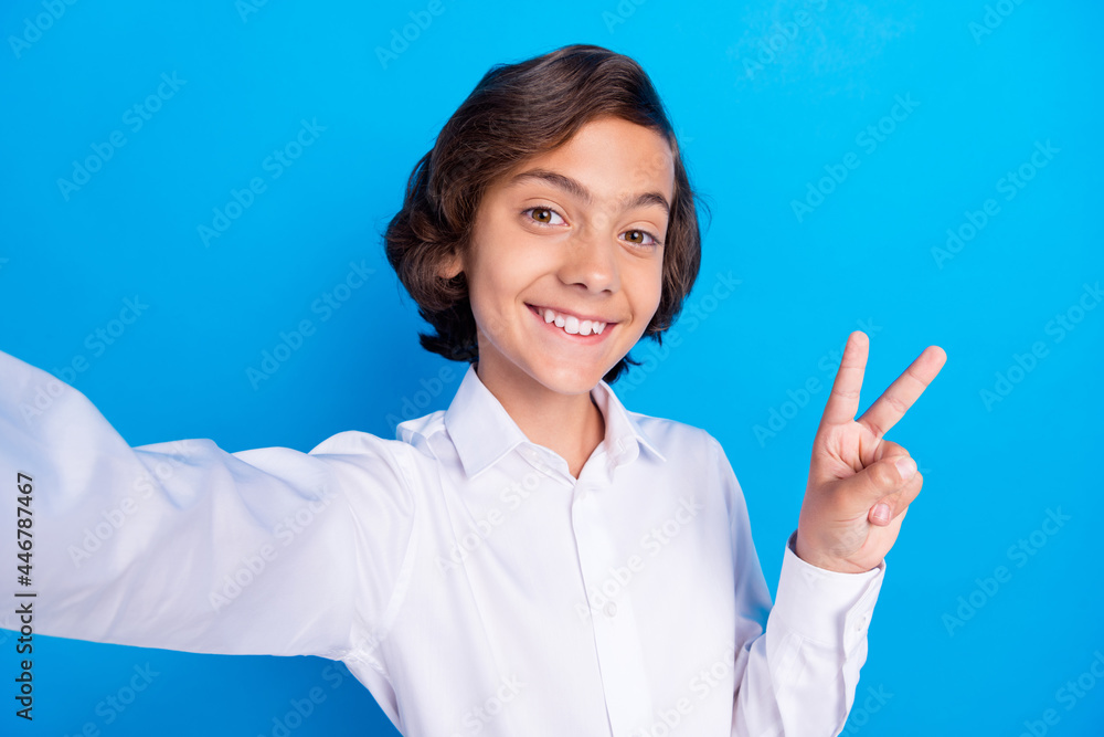Photo of sweet attractive school boy wear formal outfit smiling recording video showing v-sign isolated blue color background Photo of sweet attractive school boy wear formal outfit smiling recording video showing v-sign isolated blue color background