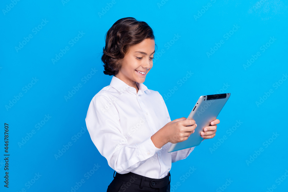 Photo of cute funny school boy wear formal outfit smiling looking modern device isolated blue color background Photo of cute funny school boy wear formal outfit smiling looking modern device isolated blue color background