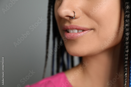 Young woman with nose piercing on grey background, closeup