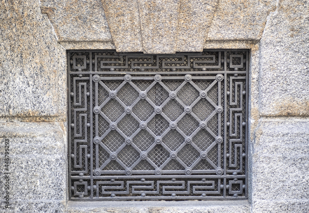 wrought iron grate with geometric decorations on the stone facade of a building wrought iron grate with geometric decorations on the stone facade of a building